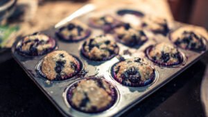 Close up of tall baker-style sourdough discard muffins with craggy tops and sparkling sugar in a muffin tin.