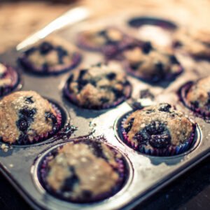 Close up of tall baker-style sourdough discard muffins with craggy tops and sparkling sugar in a muffin tin.