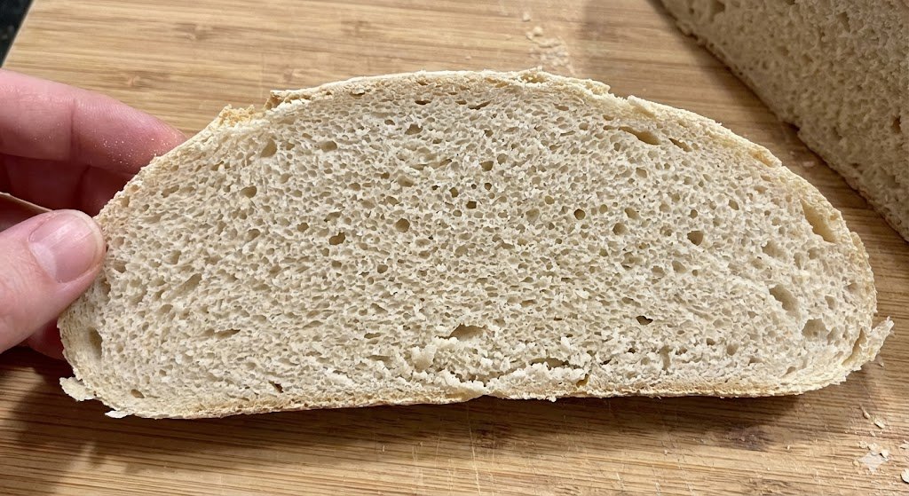 Overproofed sourdough slice with uniform, sponge-like texture, fragile crumb, and flat shape.